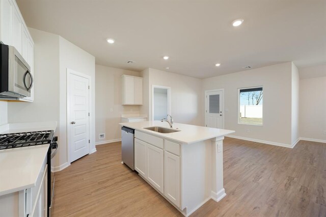 kitchen with a sink, light wood-style floors, stainless steel appliances, a center island with sink, and white cabinetry
