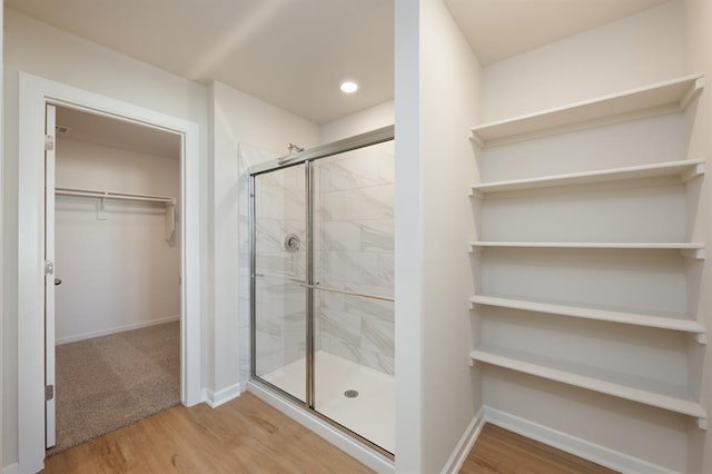 full bath with baseboards, wood finished floors, a shower stall, and a walk in closet