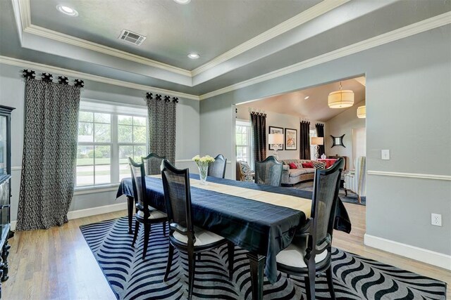 dining space featuring crown molding, a raised ceiling, light wood finished floors, baseboards, and visible vents