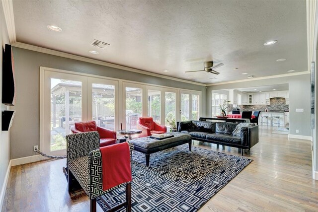 living area with baseboards, ornamental molding, light wood finished floors, and ceiling fan