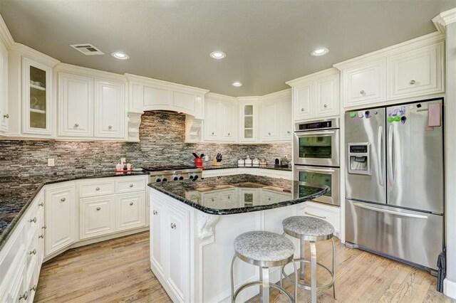 kitchen featuring a breakfast bar area, visible vents, appliances with stainless steel finishes, dark stone countertops, and light wood-style floors
