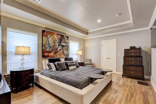 bedroom featuring ornamental molding, light wood-style flooring, and a tray ceiling
