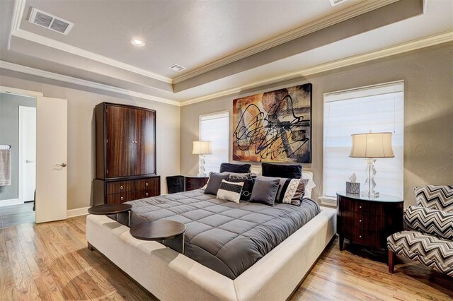 bedroom featuring visible vents, light wood finished floors, crown molding, and a tray ceiling