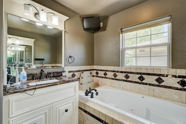full bathroom with a tub with jets, a textured wall, and vanity