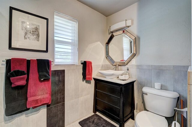 bathroom featuring vanity, wainscoting, toilet, and tile walls