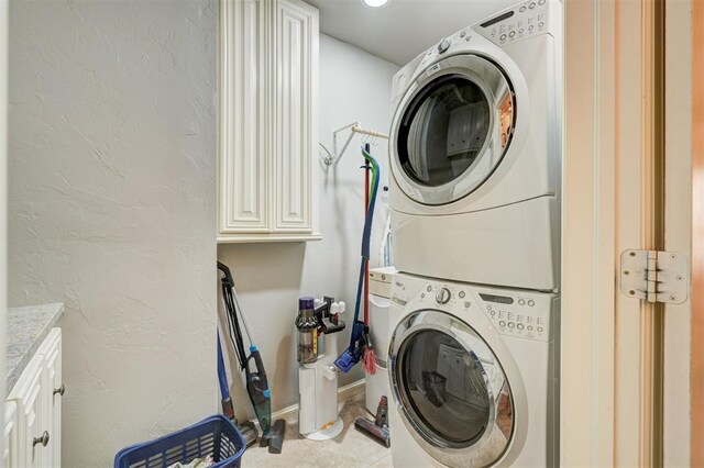 laundry room featuring baseboards, cabinet space, stacked washing maching and dryer, and a textured wall