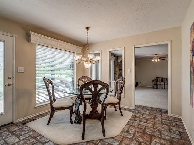 dining space with a textured ceiling, ceiling fan with notable chandelier, brick floor, and baseboards