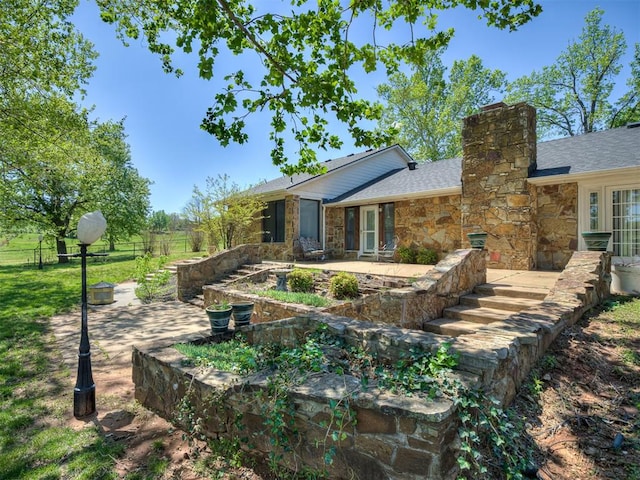 rear view of house with a patio, fence, stone siding, and a chimney