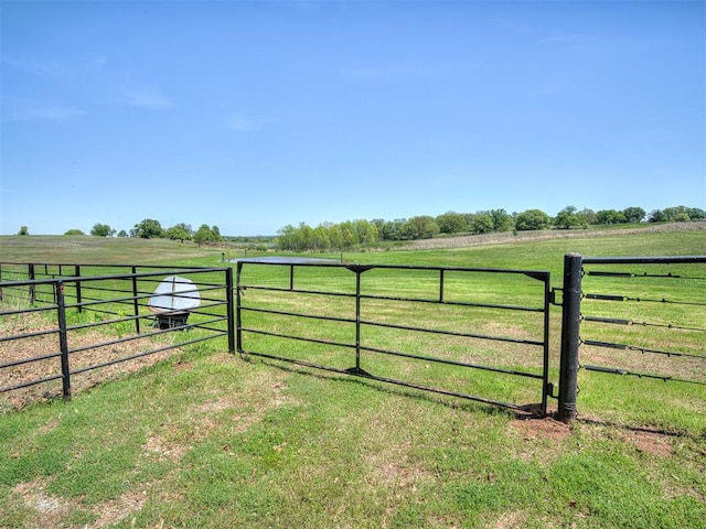 view of gate with fence, a rural view, and a lawn