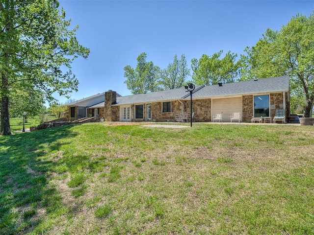 rear view of property featuring a yard, stone siding, french doors, and a garage