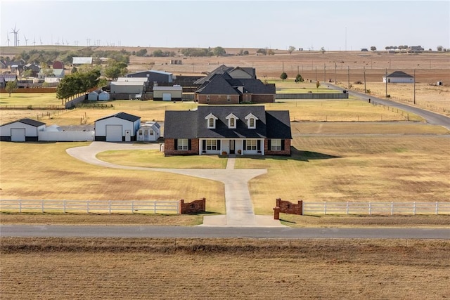 view of front of home featuring a front lawn, a detached garage, driveway, fence, and a rural view