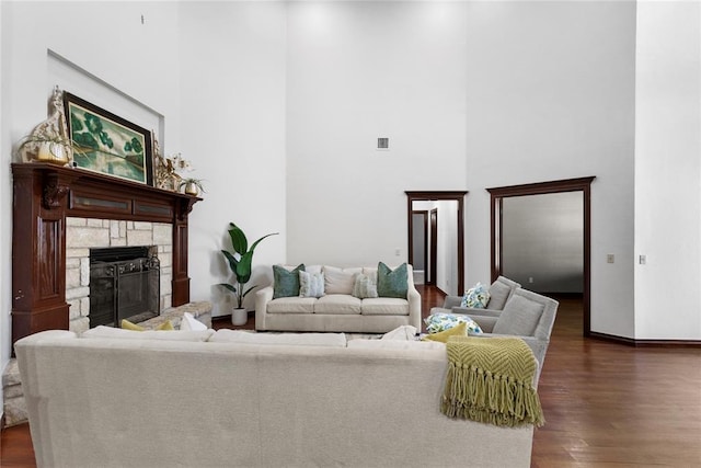 living area featuring a stone fireplace, baseboards, a high ceiling, dark wood-style flooring, and visible vents
