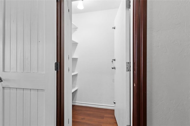 hall featuring baseboards, a textured wall, and wood finished floors