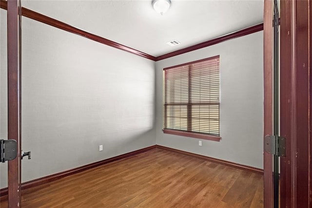 empty room featuring visible vents, baseboards, wood finished floors, and ornamental molding
