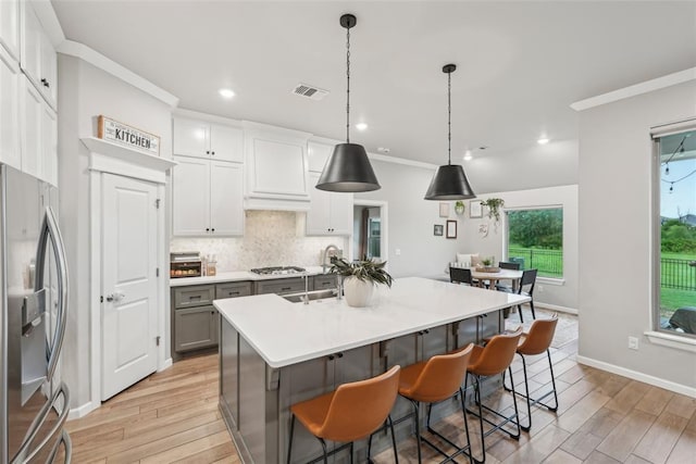 3320 Lola Ct, Moore, OK 73160 - kitchen featuring a kitchen island with sink, crown molding, tasteful backsplash, stainless steel appliances, and light wood-style flooring