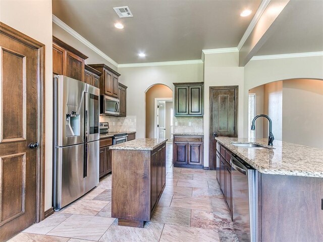 kitchen with a sink, arched walkways, a center island with sink, and stainless steel appliances
