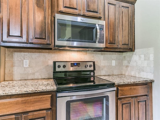 kitchen featuring appliances with stainless steel finishes, dark brown cabinetry, backsplash, and light stone countertops