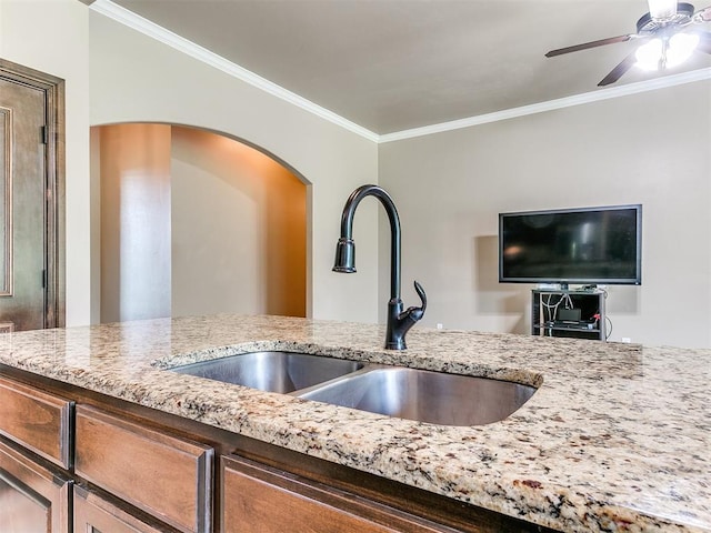 kitchen featuring crown molding, ceiling fan, light stone counters, and a sink