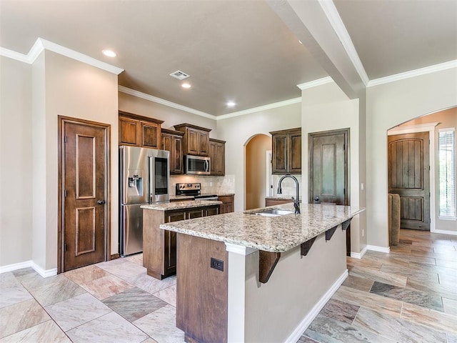 kitchen with appliances with stainless steel finishes, arched walkways, a sink, baseboards, and an island with sink
