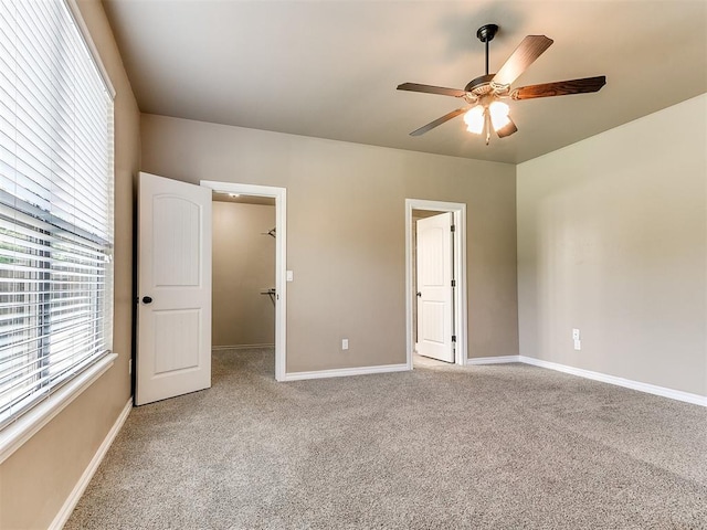 unfurnished bedroom with light colored carpet, a ceiling fan, baseboards, and a walk in closet