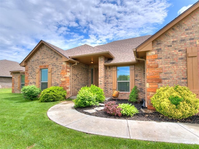 property entrance with a lawn, roof with shingles, and brick siding