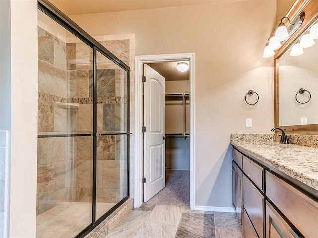 full bath with vanity, baseboards, a spacious closet, and a shower stall