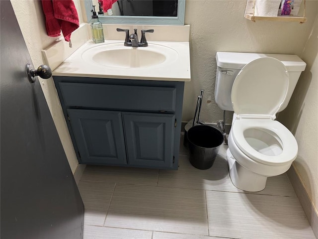 bathroom featuring toilet, tile patterned floors, a textured wall, and vanity