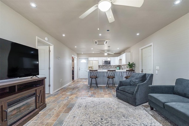 living room featuring ceiling fan, baseboards, stone tile flooring, and recessed lighting