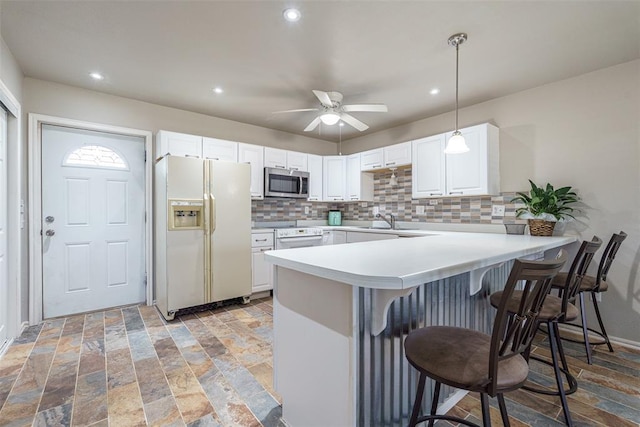 kitchen with a peninsula, a breakfast bar area, decorative backsplash, and white appliances