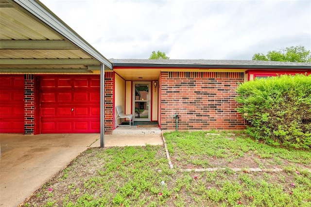 view of exterior entry with a garage, concrete driveway, and brick siding