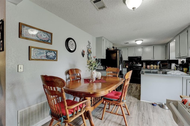 dining space with visible vents, a textured ceiling, and light wood finished floors
