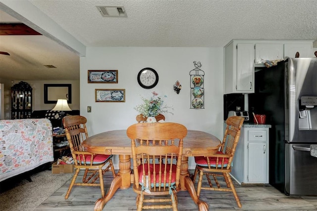 dining area with visible vents, a textured ceiling, and light wood finished floors