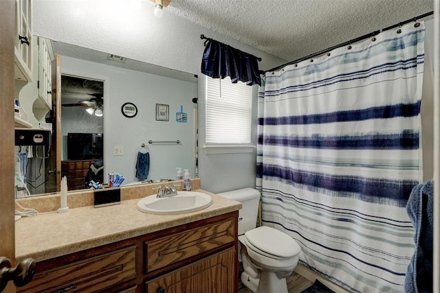 bathroom with ceiling fan, vanity, toilet, a textured ceiling, and visible vents