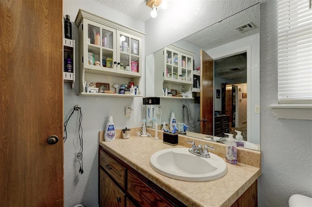 bathroom featuring vanity, a textured ceiling, a textured wall, and visible vents