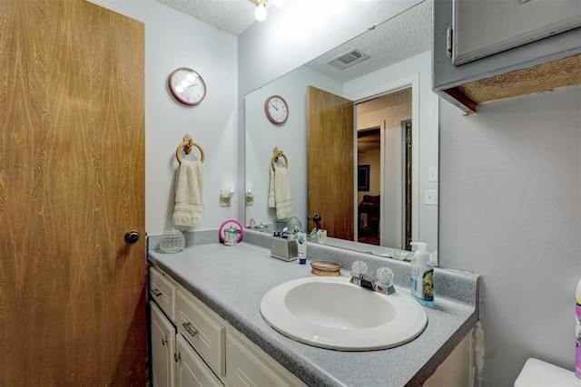 bathroom featuring toilet, a textured ceiling, visible vents, and vanity