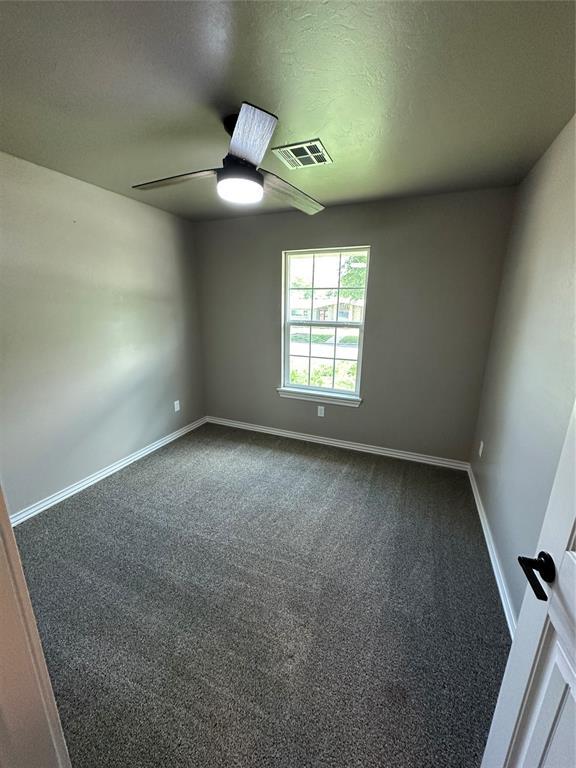 spare room with a ceiling fan, dark colored carpet, baseboards, and visible vents