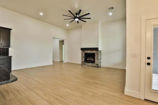 unfurnished living room with visible vents, a fireplace, baseboards, a ceiling fan, and light wood finished floors