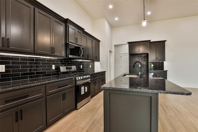 kitchen with a sink, dark stone countertops, stainless steel appliances, backsplash, and a center island with sink