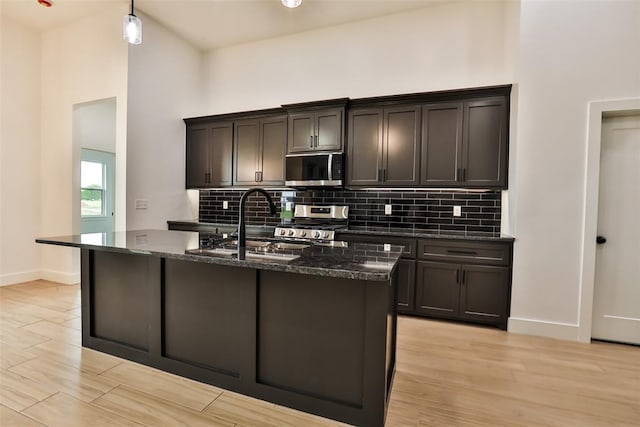kitchen with light wood-style floors, a sink, dark stone countertops, and appliances with stainless steel finishes
