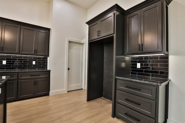 kitchen featuring backsplash, dark brown cabinetry, light wood finished floors, and dark stone countertops