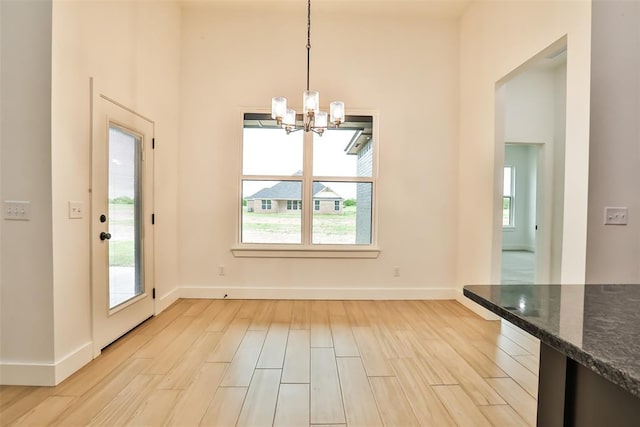 unfurnished dining area featuring baseboards, a chandelier, a healthy amount of sunlight, and light wood-type flooring