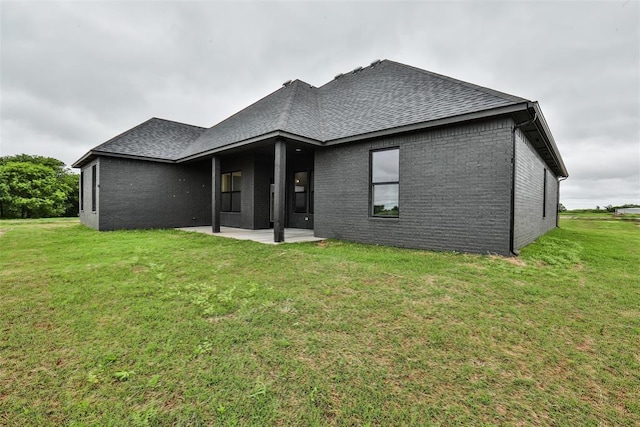 back of property with brick siding, a patio, roof with shingles, and a lawn