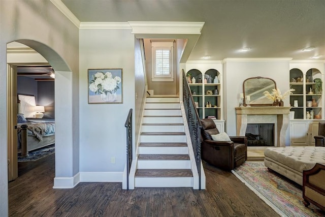staircase with crown molding, built in features, wood finished floors, baseboards, and a high end fireplace