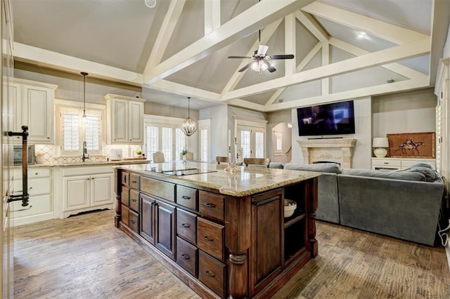 kitchen with light stone counters, black electric stovetop, a sink, high vaulted ceiling, and cream cabinetry