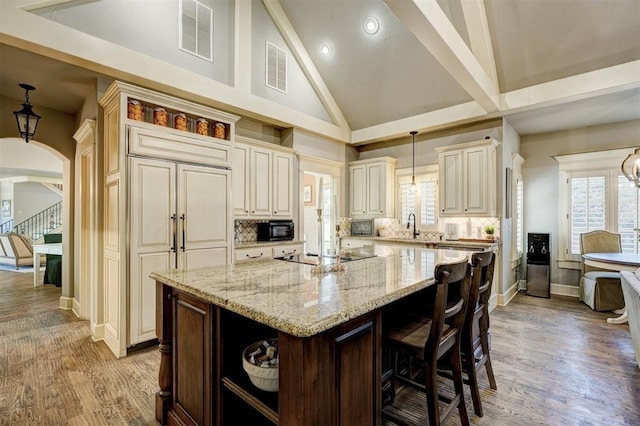 kitchen with open shelves, light stone counters, visible vents, a center island with sink, and black appliances