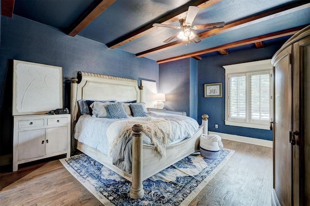 bedroom featuring baseboards, a ceiling fan, beamed ceiling, and wood finished floors