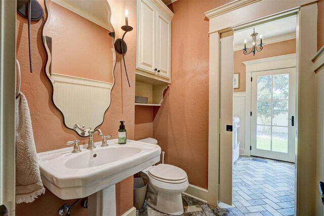 bathroom with brick floor, a sink, toilet, a notable chandelier, and ornamental molding