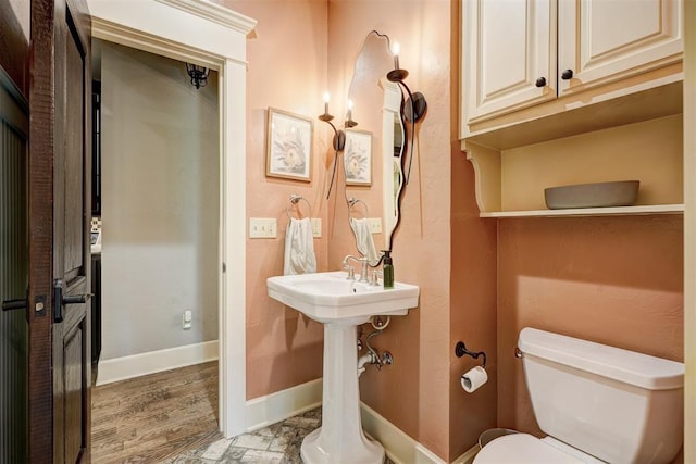 half bathroom featuring baseboards, wood finished floors, and toilet