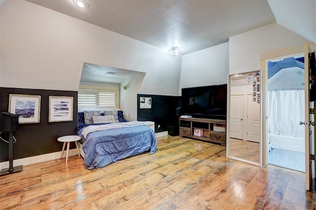 bedroom featuring visible vents, baseboards, connected bathroom, lofted ceiling, and hardwood / wood-style floors