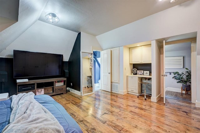 interior space featuring visible vents, baseboards, built in study area, light wood finished floors, and vaulted ceiling